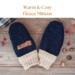 Pair of warm & cozy navy blue fleece baby mittens with beige ribbed cuffs on rustic wood background — thumbless winter mittens for toddlers.