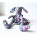 Handmade gray wool rabbit doll in floral dress, sitting with floppy ears and soft wool texture.