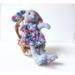 Handmade gray wool rabbit doll named Josie wearing a bright floral dress, seated on a rustic twig chair—eco-friendly heirloom toy.