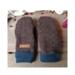 Pair of handmade women’s brown fleece mittens with navy cuffs and leather warmth tag, displayed flat on rustic wood background.