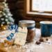 Winter Hot Cocoa Jar beside blue mug, snow-dusted table, and pine tree lights in rustic cabin setting.