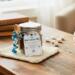 Cozy Winter Hot Cocoa Jar on wooden table near window with marshmallows and books in soft natural light.