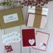 A handmade card kit to make 12 embossed valentine's cards, with pink and red cardstock, "love you" stamped sentiments and cardstock bows.