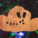 Handmade wooden Christmas tree ornament shaped like a cowboy hat, featuring a sprig of holly tucked into the hat band, hand cut holly leaf cutouts, and round berry accents.