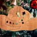 Handmade wooden Christmas tree ornament shaped like a cowboy hat, featuring a sprig of holly tucked into the hat band, hand cut holly leaf cutouts, and round berry accents.