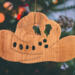 Handmade wooden Christmas tree ornament shaped like a cowboy hat, featuring a sprig of holly tucked into the hat band, hand cut holly leaf cutouts, and round berry accents.