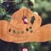 Handmade wooden Christmas tree ornament shaped like a cowboy hat, featuring a sprig of holly tucked into the hat band, hand cut holly leaf cutouts, and round berry accents.
