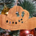 Handmade wooden Christmas tree ornament shaped like a cowboy hat, featuring a sprig of holly tucked into the hat band, hand cut holly leaf cutouts, and round berry accents.