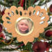Wooden heart-shaped ornament with scalloped edges and an oak grain finish, featuring a removable round gold frame that holds a photo of a smiling blonde child.