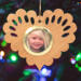 Wooden heart-shaped ornament with scalloped edges and an oak grain finish, featuring a removable round gold frame that holds a photo of a smiling blonde child.