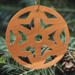 A handmade wooden Christmas tree ornament, circular in shape, crafted from light brown wood with a natural grain pattern. It features an intricate, symmetrical cutout design resembling a star or snowflake, with multiple pointed shapes radiating from a central hole. The ornament is attached to a small metal hook for hanging, showcasing its rustic and festive craftsmanship.