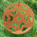 A handmade wooden Christmas tree ornament, circular in shape, crafted from light brown wood with a natural grain pattern. It features an intricate, symmetrical cutout design resembling a star or snowflake, with multiple pointed shapes radiating from a central hole. The ornament is attached to a small metal hook for hanging, showcasing its rustic and festive craftsmanship.