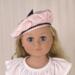 Blonde 18 inch doll wearing a pink beret/hat with black trimmings