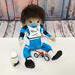 21 inch fully handmade cloth boy doll in light tan skin tone with dark brown hair and brown eyes. Wearing a blue and white racing jersey with matching riding pants, motocross boots and chest protector. Has magnetic bottle, pacifier, and toy dirtbike