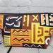 Back of a brown orange and yellow geometric African print cosmetic bag with a gunmetal zipper.